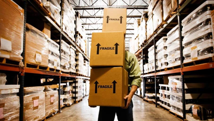 Warehouse worker carrying a stack of fragile-labelled boxes