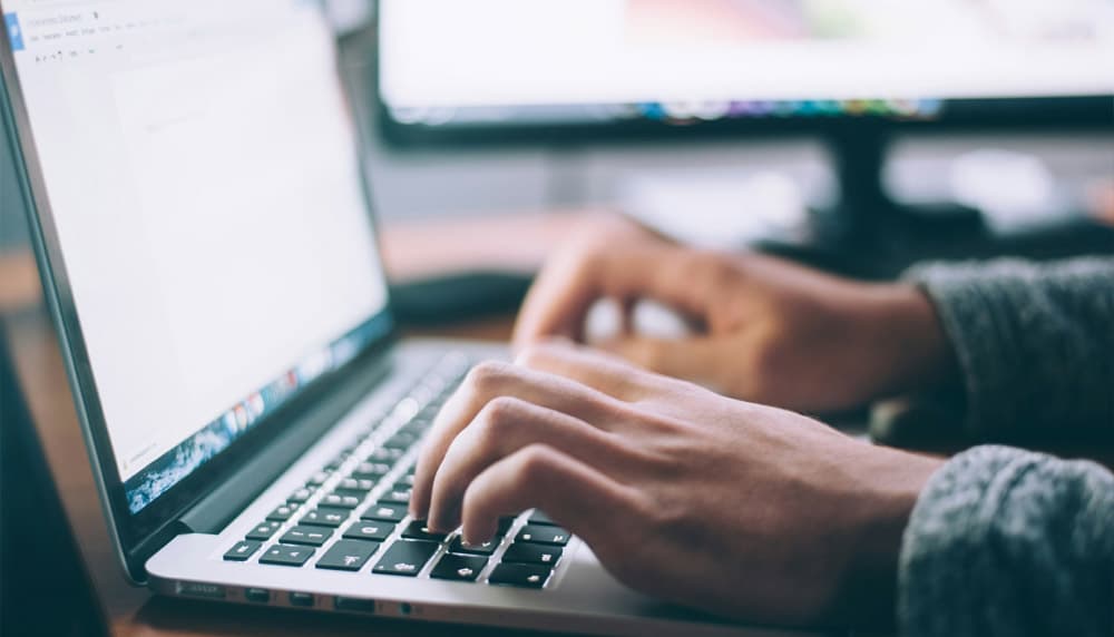 Hands typing on a laptop while comparing carrier shipping rates