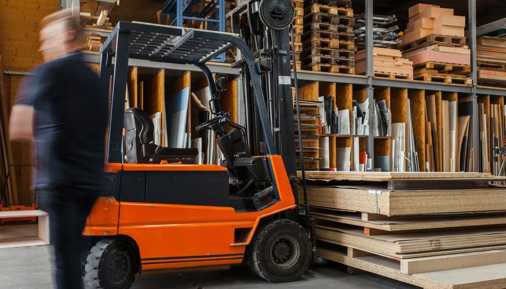 Forklift moving stock between racks of shelved inventory