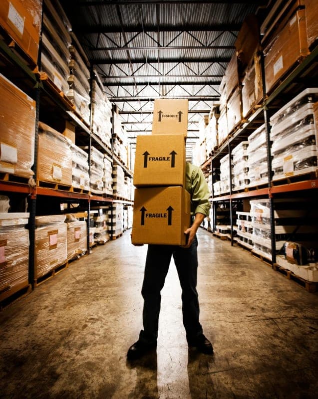 Warehouse worker carrying a stack of boxes down an aisle