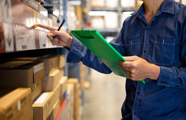 Warehouse worker with a clipboard counting stock on a shelf